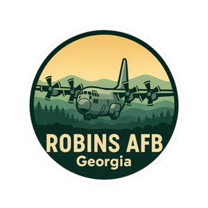 May include: A circular sticker featuring a stylized illustration of a military transport aircraft flying over a forest and mountains. The text "ROBINS AFB Georgia" is displayed in a bold font.