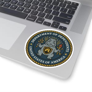 Op de afbeelding: Een ronde sticker met een cartoon nijlpaard met een fakkel en een takje bladeren. Het nijlpaard draagt een schild met een huisafbeelding. De sticker heeft de tekst "DEPARTMENT OF DEPENDENTS" en "UNITED STATES OF AMERICA".