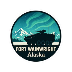 May include: A circular sticker with a dark silhouette of a military vehicle set against a backdrop of mountains, aurora borealis, and a snowy landscape. The text "FORT WAINWRIGHT Alaska" is at the bottom.