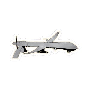May include: A gray and white drone with a propeller on the front and a missile attached to the bottom. The drone is flying in the air.