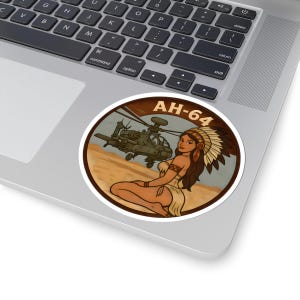 May include: Round sticker featuring a vintage-style illustration. The design includes a military helicopter, a Native American woman, and the text "AH-64" in a brown and tan color scheme. The sticker is placed on a laptop.