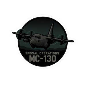 May include: A sticker featuring a dark grey MC-130 military aircraft illustration. The aircraft is centered within a black circular frame, with the words "SPECIAL OPERATIONS" and "MC-130" in white text below the plane. The background is a dark green.