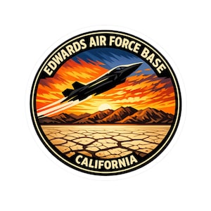 May include: A circular sticker featuring the text "EDWARDS AIR FORCE BASE CALIFORNIA". The design includes a black jet soaring across a sunset sky over a desert landscape.
