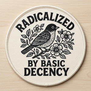 May include: Round patch with the text "RADICALIZED BY BASIC DECENCY" in black, surrounding a black and white illustration of a bird perched on a flowering branch. The patch has a cream-colored background and a stitched border.
