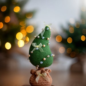 May include: A green crocheted Christmas tree with a brown crocheted base and a yellow ribbon. The tree is decorated with white and blue beads.