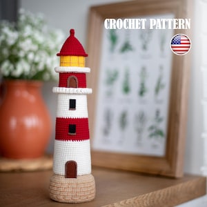Può includere: Un faro all'uncinetto con tetto rosso, lanterna gialla e strisce rosse e bianche alternate. Il faro presenta piccoli dettagli di porta e finestra marroni. La base è di colore beige chiaro. Il testo "CROCHET PATTERN" è visibile.