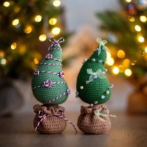 May include: Two crocheted Christmas trees with brown burlap bases. One tree is decorated with red and white twine and the other with white beads and a yellow ribbon.