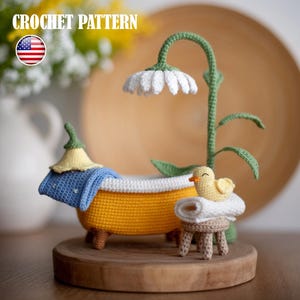 Puede incluir: Escena de baño en miniatura tejida a ganchillo con una bañera amarilla, una lámpara en forma de margarita y un patito sobre un taburete. Todo sobre una base de madera. El texto "CROCHET PATTERN" es visible.