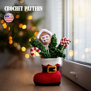 Puede incluir: Patrón de crochet para una bota de Navidad llena de un árbol verde, una casa de jengibre y bastones de caramelo. La bota es roja con un puño negro y un cinturón amarillo.