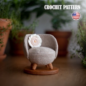 Puede incluir: Un sillón de crochet con un cojín de flor blanca, sentado sobre una base de madera. El sillón es beige y tiene un asiento redondo. El cojín de la flor tiene un pequeño botón redondo de color melocotón en el centro.
