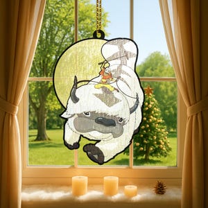 Puede incluir: Colgante decorativo para ventana con una imagen de dibujos animados de un bisonte blanco con un personaje montado en su espalda. El bisonte tiene cuernos y patas negras. El fondo es un círculo amarillo con una cadena dorada para colgar.