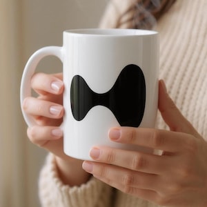 May include: A white ceramic mug with a black abstract design. The mug has a curved handle and is filled with a hot beverage, as indicated by the rising steam. The mug is held by a person wearing a beige sweater.