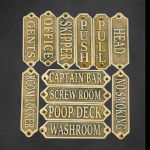 Puede incluir: Una colección de letreros de latón de estilo vintage con varios textos grabados. Los letreros incluyen "GENTS", "OFFICE", "SKIPPER", "PUSH", "PULL", "HEAD", "ROOM LOCKER", "CAPTAIN BAR", "SCREW ROOM", "POOP DECK", "WASHROOM" y "NO SMOKING".