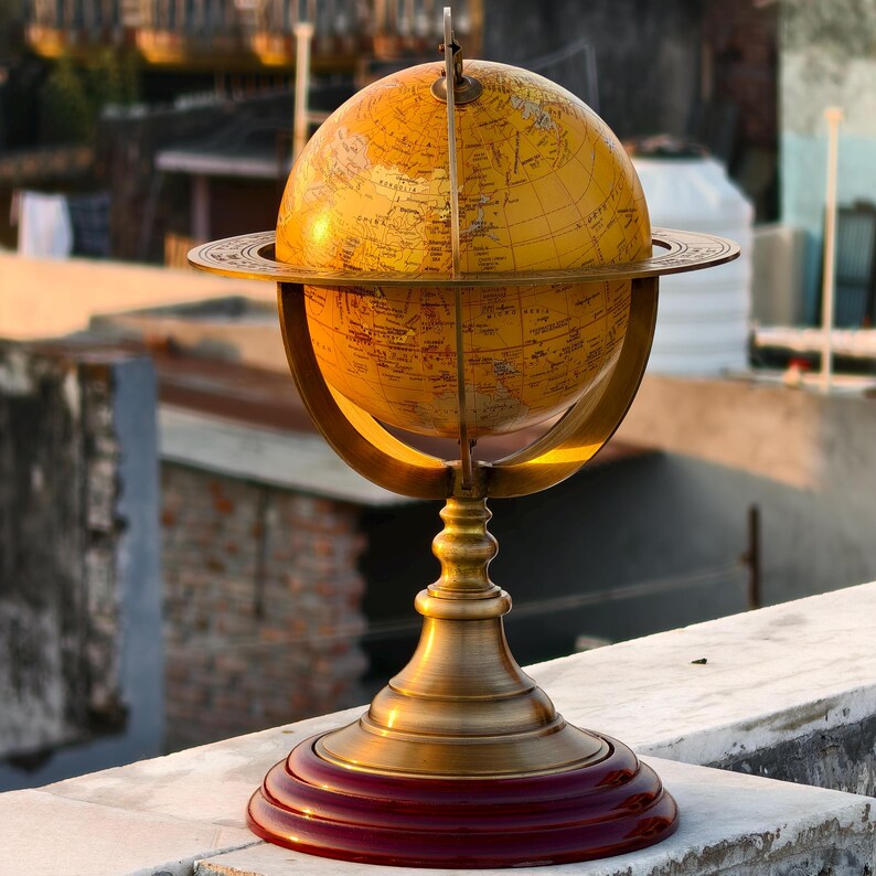 May include: A vintage-style globe with a yellowed map, mounted on a brass stand with a dark red base. The globe is held by a brass meridian and sits on a decorative stand. The globe is a classic decorative piece.