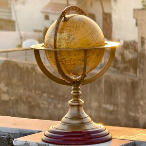 May include: A vintage-style globe with a gold finish, mounted on a brass stand with a red base. The globe features detailed geographical markings and is supported by a brass meridian and horizon ring. The overall height is approximately 12 inches.