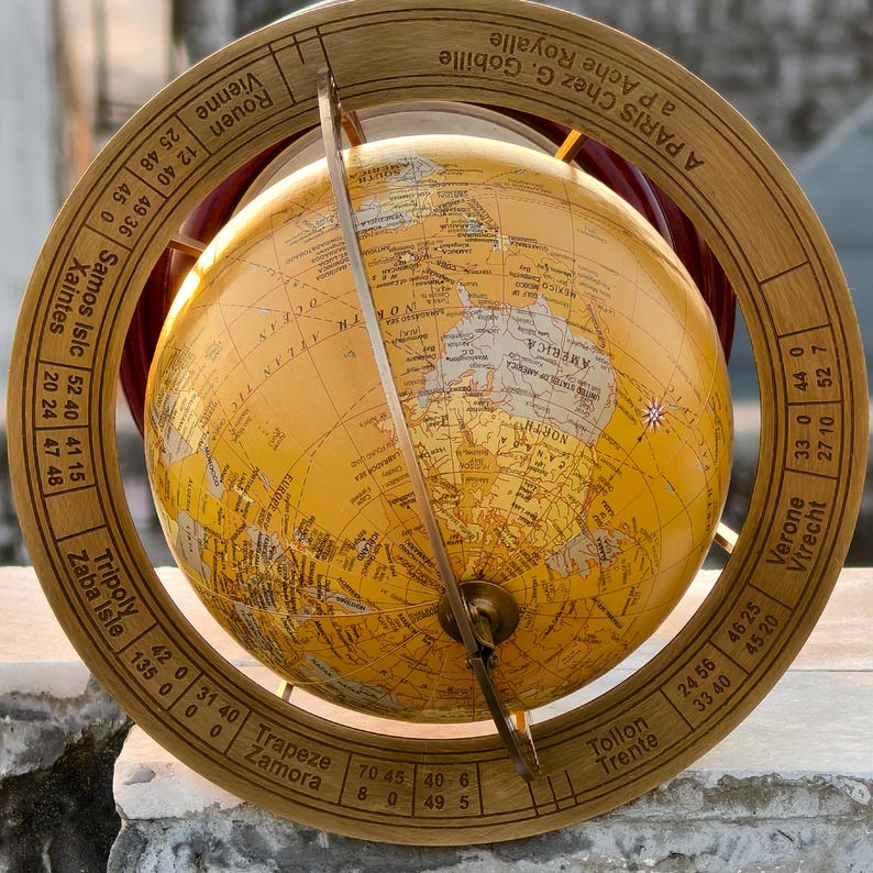 May include: A vintage-style globe with a yellowed map, set within a wooden frame. The frame features engraved text and coordinates. A metal meridian and a brass-colored stand complete the antique aesthetic. The globe is a decorative item.