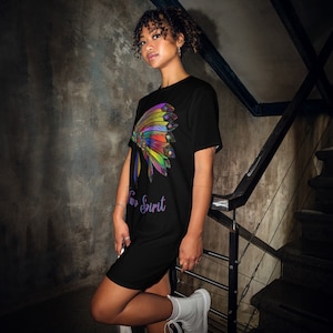 Könnte beinhalten: Schwarzes T-Shirt-Kleid mit einem bunten indianischen Kopfschmuck-Design auf der linken Seite. Der Text "Two Spirit" ist darunter in Lila gedruckt. Das Kleid ist knielang.