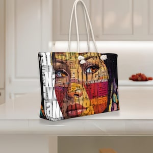 May include: A rectangular tote bag with white rope handles featuring a graphic print of a face composed of layered text. The artwork uses warm tones of orange, red, and yellow, with the word Native repeated throughout the design in various fonts.
