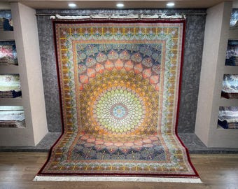 Könnte beinhalten: Ein großer, verzierter Teppich mit einem zentralen floralen Medaillon-Design. Der Teppich hat eine lebendige Farbpalette aus Orange, Gelb, Grün und Blau, mit komplizierten Mustern und einem dunkelroten Rand. Der Teppich wird in Innenräumen ausgestellt.