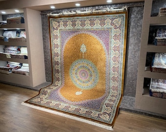 Könnte beinhalten: Ein großer, verzierter Teppich mit einem zentralen Medaillon-Design in Gold-, Lila- und Blautönen. Der Teppich weist komplizierte Blumenmuster und einen detaillierten Rand auf. Der Teppich wird in einem Geschäft ausgestellt, um seine Größe und sein Design zu präsentieren.