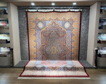 Könnte beinhalten: Ein großer, verzierter Teppich mit einem zentralen Medaillon-Design. Der Teppich weist ein komplexes Muster in Blau-, Gold-, Rot- und Cremetönen auf. Der Teppich wird in einem Ausstellungsraum präsentiert, der seine komplizierten Details und seine Handwerkskunst hervorhebt.