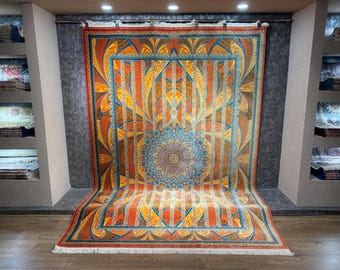Könnte beinhalten: Ein großer, rechteckiger Teppich mit einem zentralen Mandala-Design. Der Teppich hat eine lebendige Farbpalette aus Orange, Blau und Gold. Das Design umfasst geometrische Muster und florale Motive und schafft ein visuell reichhaltiges und detailliertes Textil.