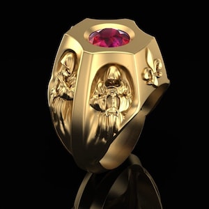 Könnte beinhalten: Ein goldener Ring mit einem roten Edelstein in der Mitte. Der Ring zeigt drei Kapuzenfiguren mit Schwertern und ein Fleur-de-lis-Design.