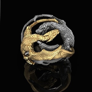 May include: A silver and gold ring featuring two intertwined dragons. The dragons are facing each other with their tails wrapped around each other. The ring is a statement piece with intricate details.
