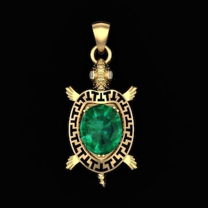 Op de afbeelding: Een gouden schildpad hanger met een groene edelsteen en een zwart-gouden geometrisch ontwerp.