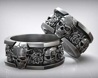 Op de afbeelding: Twee zilveren ringen met schedels en rozen. De ringen zijn breed en hebben een herhalend patroon van schedels en rozen.