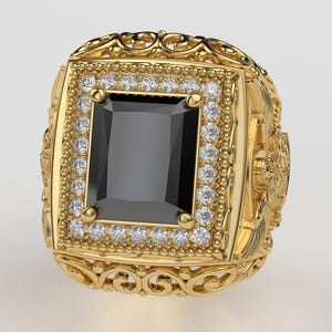 Puede incluir: Un anillo dorado con una gran piedra negra rectangular en el centro. El anillo est&aacute; adornado con peque&ntilde;as piedras preciosas transparentes alrededor de la piedra negra y presenta intrincados detalles de filigrana y elementos decorativos.