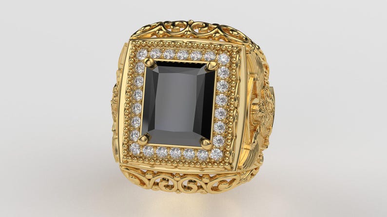 Puede incluir: Un anillo dorado con una gran piedra negra rectangular en el centro. El anillo est&aacute; adornado con peque&ntilde;as piedras preciosas transparentes alrededor de la piedra negra y presenta intrincados detalles de filigrana y elementos decorativos.