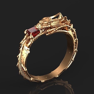 Puede incluir: Un anillo dorado con un diseño de dragón. La cabeza del dragón sostiene una gema roja rectangular. El anillo tiene detalles intrincados, incluyendo escamas y patrones decorativos a lo largo de la banda. El anillo se muestra sobre un fondo oscuro.