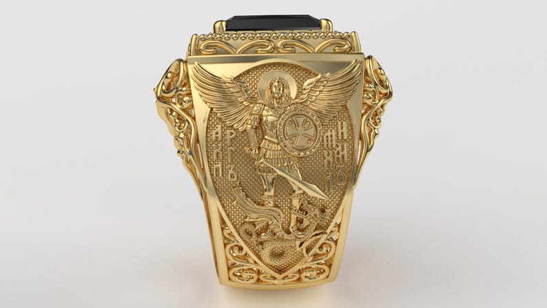 Puede incluir: Un anillo dorado con un dise&ntilde;o ornamentado. El anillo presenta un escudo central con un &aacute;ngel sosteniendo una espada y un escudo. El anillo tiene una piedra negra rectangular en la parte superior y est&aacute; muy detallado con volutas.