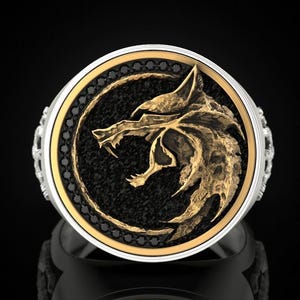 May include: A silver ring with a black and gold wolf head design. The wolf head is surrounded by black diamonds.