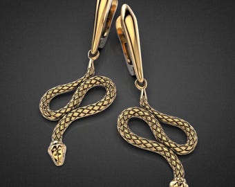 May include: A pair of gold-colored snake earrings. Each earring features a stylized snake design with a textured, scale-like pattern. The snake's head is detailed, and the earrings have a hook closure.