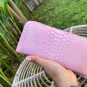 Peut inclure: Un portefeuille en cuir de serpent rose avec une fermeture &eacute;clair.