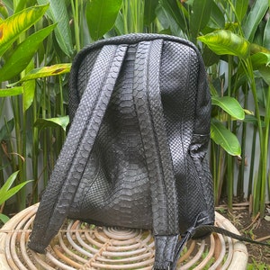 May include: Black leather backpack with a snakeskin pattern. The backpack has a zip closure and adjustable straps.