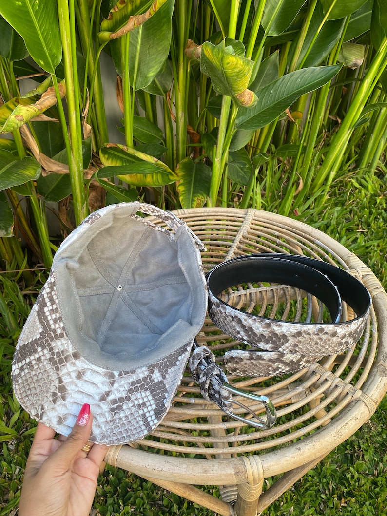 May include: A gray and white snakeskin baseball cap and a matching snakeskin belt with a silver buckle.
