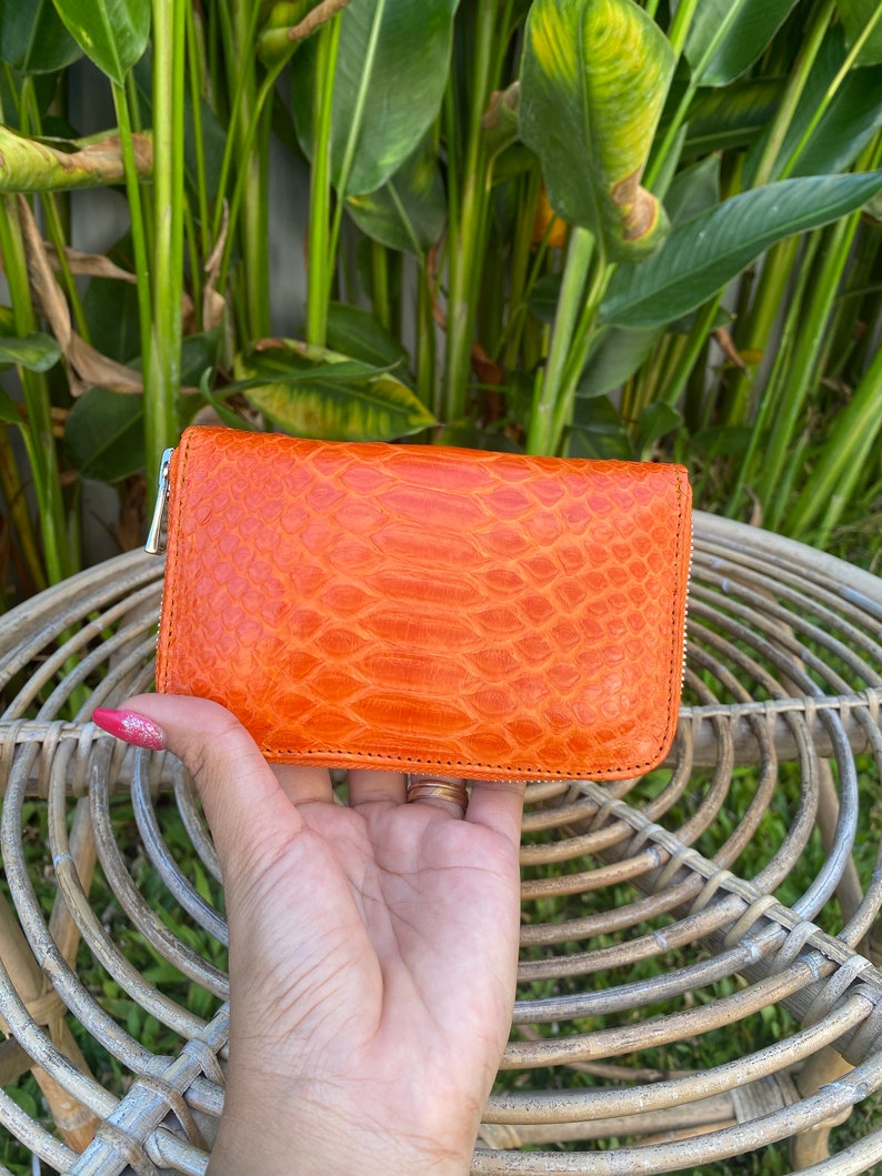 May include: A small orange leather wallet with a zipper closure and a textured snakeskin pattern.