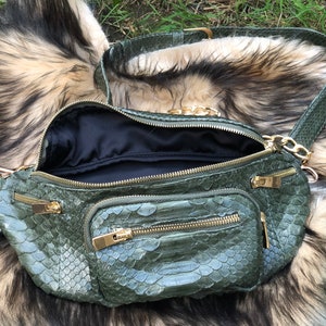 Puede incluir: Una ri&ntilde;onera de piel de serpiente verde con herrajes dorados y una correa de cadena. La bolsa tiene varios compartimentos con cremallera.