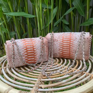 May include: Two small, orange and white snakeskin purses with silver chain straps. The purses are sitting on a woven wicker stool.