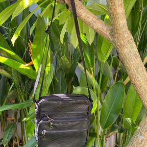 May include: A black leather crossbody bag with a textured snakeskin pattern. The bag has two zippered compartments and a long adjustable strap.