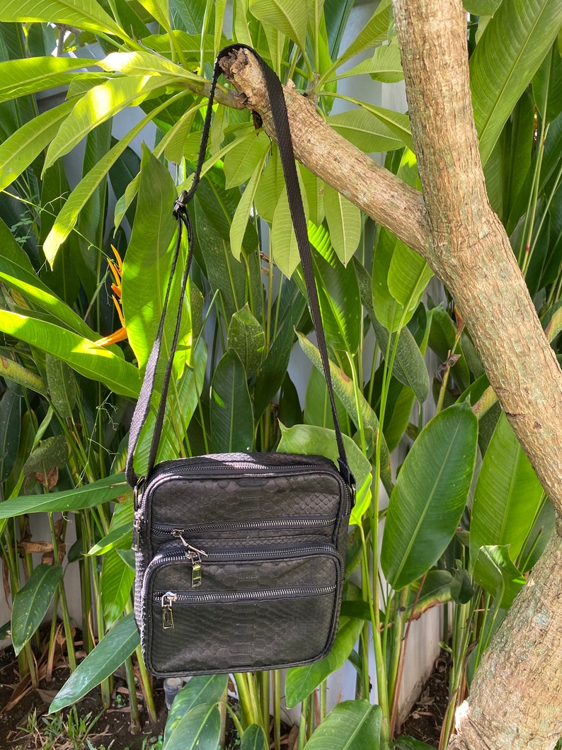 May include: A black leather crossbody bag with a textured snakeskin pattern. The bag has two zippered compartments and a long adjustable strap.