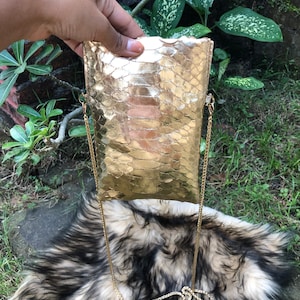 May include: A gold metallic snakeskin clutch bag with a gold chain strap.