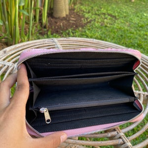 Peut inclure: Un portefeuille zipp&eacute; rose avec un int&eacute;rieur noir et plusieurs compartiments. Le portefeuille est ouvert et l'int&eacute;rieur est visible.