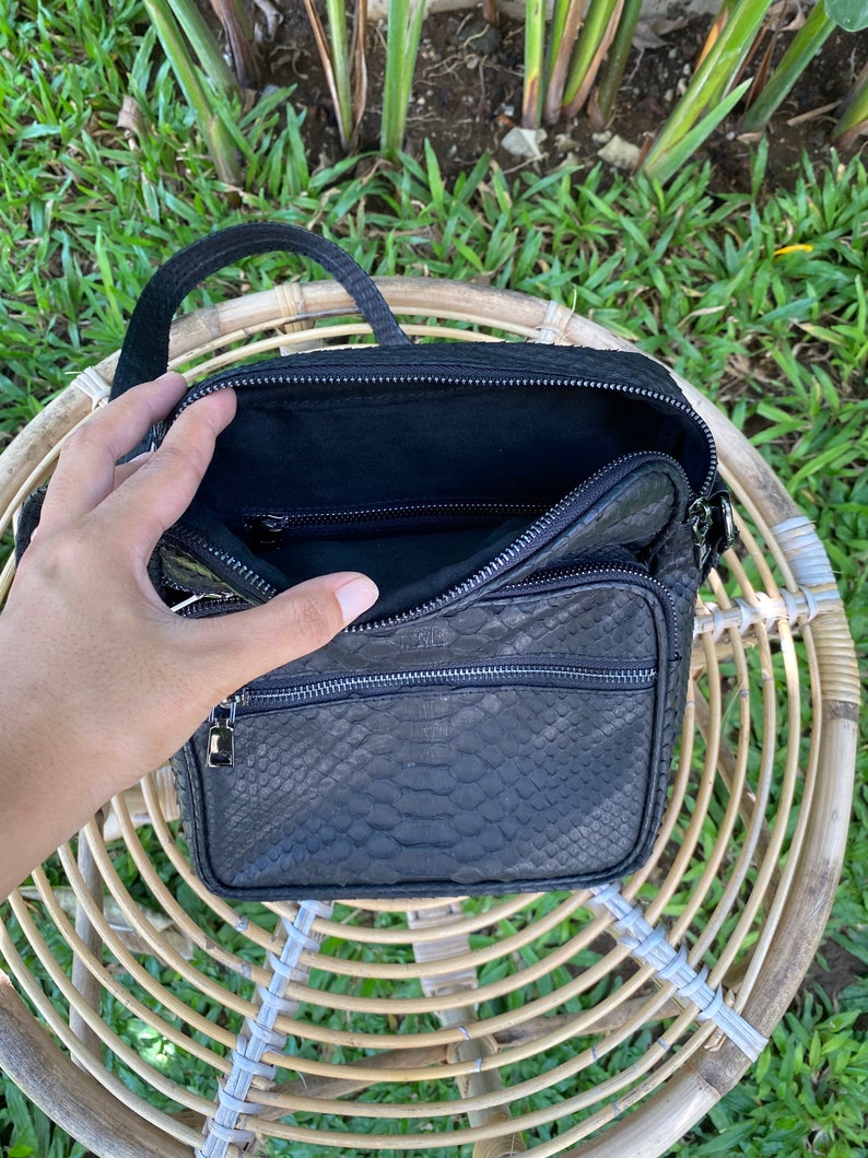 May include: Black leather crossbody bag with a snakeskin pattern and multiple zippered compartments.