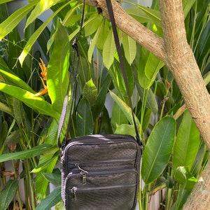 May include: A black leather crossbody bag with a snakeskin pattern and multiple zippered compartments.