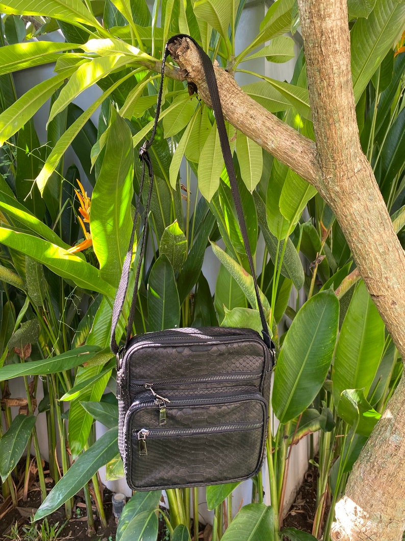 May include: A black leather crossbody bag with a snakeskin pattern and multiple zippered compartments.