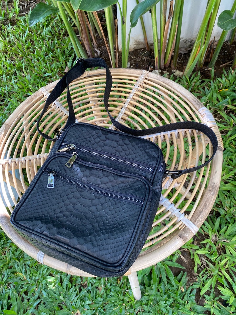 May include: Black leather crossbody bag with a snakeskin pattern and multiple zippered compartments.